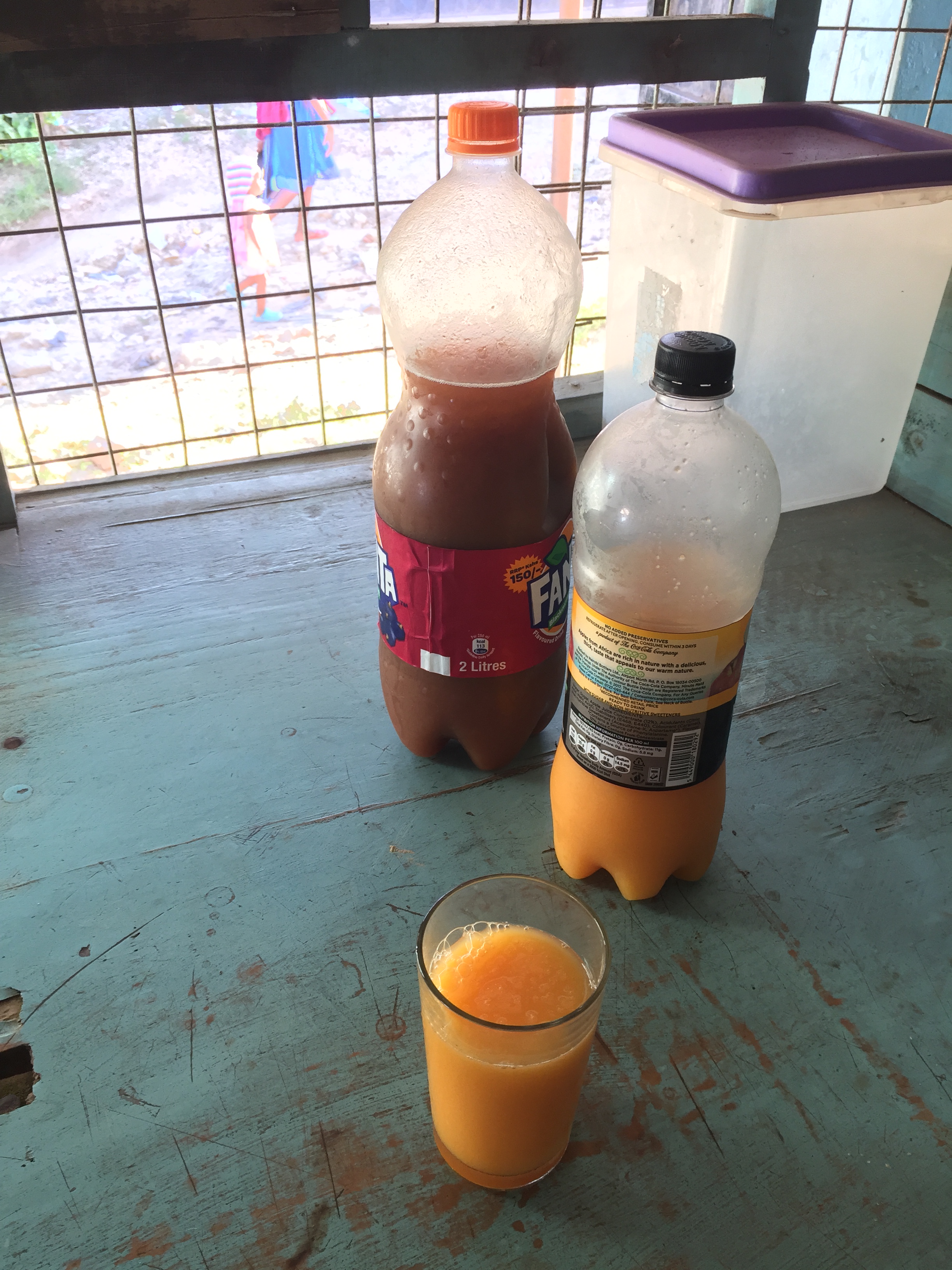 Two plastic bottles, one filled with tamarind juice and the other passionfruit, with a glass in foreground filled with passionfruit juice